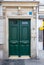 Green painted wooden door and framed panels with shiny brass door handles. Antique building with sculptural arch with lion head