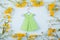 Green paper origami dress on hanger surrounded with yellow and white little flowers on light mint background.