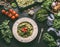 Green pasta with raw kale pesto and grilled tomatoes in plate with fork on kitchen table with ingredients. Vegan food. Healthy