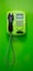 Green payphone with a black tube and blue display