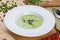 Green pea soup in a white plate. Cream soup on wooden table. Flat lay: soup, peas, tomatoes.