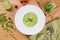 Green pea soup in a white plate. Cream soup on wooden table. Flat lay: soup, peas, tomatoes.