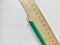 Green pencil and wooden ruler with metric system rests on a white checkered exercise book without notes