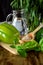 A green pepper, brans in a wooden spoon, basil, tarragon, a cucumber and water in a glass jug.