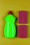 Green plastic bottle of dishwashing liquid and red sponge on greenish-yellow background close-up top view,