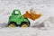 Green plastic toy souvenir excavator with orange bucket shovel and yellow wheels clears snow on a white background