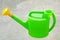 Green plastic watering can with yellow nozzle on gray concrete background. Watering pot is the simplest tool for drip