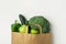 Green raw organic vegetables fruits broccoli cucumbers bell peppers apples in brown Kraft paper grocery bag on white background