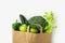 Green raw organic vegetables fruits broccoli cucumbers bell peppers apples celery in brown paper grocery bag on white background