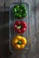 Green, red, yellow bell peppers arranged vertically in an aluminum basket on a rustic wooden floor, top view.