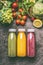 Green,red and yellow colorful organic vegetables, fruits and berries smoothies with ingredients in bottles on gray granite table