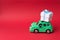 Green retro toy car delivering white gift on red background with copy space
