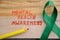 The green ribbon cross with red writing mental health awareness concept on the wooden background