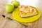 Green ripe apples, piece of apple pie in yellow plate, knife on table