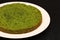Green round spinach mint cake on a white plate on a black background