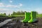 Green rubber boots in the mud next to a puddle on a wet country road.