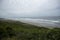 Green rugged hills leading down to coastal scenery by the ocean and wide gray sky