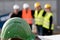 Green safety helmet on foreground. Group of four construction workers posing on out of focused background