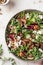 Green salad with feta cheese, arugula, mushrooms, walnut in ceramic bowl on textured background close up. Healthy summer