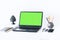 Green screen laptop, concrete holder with pencils and pens, notebook, smartphone, glasses and black paperweight on white table,
