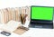 Green screen laptop, pile if books, notebook, smartphone, glasses and pencils in holder on white table, education concept