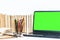 Green screen laptop, pile if books, notebook, smartphone, glasses and pencils in holder on white table, education concept