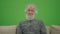 Green Screen. An Old Man with a Gray Beard Listens to Music on Headphones.