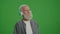 Green Screen. An Old Man with a Gray Beard Listens to Music on Headphones.