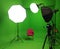 A green screen studio with complete equipment, video camera, lighting, umbrellas, bulb lighting. With a red chair. Lights On.