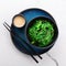 Green seaweed salad in a black bowl, peanut sauce and chopsticks on a beautiful blue plate on a white stone