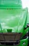 Green semi truck cab with open hood and clouds reflection