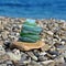 Green shades seaglass stack on rock seashore with seascape background. Sea glass pyramid beach combing