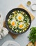 Green shakshouka with eggs, spinach, salty sheep milk cheese, celery and pepper in pan