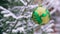 Green shiny round toy on a Christmas tree covered with snow.