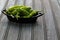 Green Shishito peppers in a metal container on wooden background