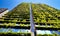 Green skyscraper building with plants growing on the facade against blue sky. Ecology and green living in city, urban environment