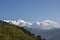 A green slope of a hill with houses on the background of the snowy mountain ridge of Annapurna under a clear blue sky