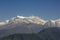 A green slope of a mountain against the backdrop of clouds and the Annapurna snow ridge under a clear blue sky