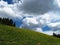 Green slope under wild clouds in blue sky