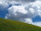 Green slope under wild clouds in blue sky