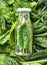 Green smoothie in bottle lies on spinach leaves background, top view