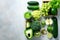 Green smoothie in glass jar with fresh organic green vegetables and fruits on grey background. Spring diet, healthy raw