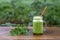 Green smoothie of parsley, avocado, honey and banana in a glass mug on a wooden table in a garden cafe, close-up