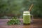 Green smoothie of parsley, avocado, honey and banana in a glass mug on a wooden table in a garden cafe, close-up