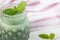 Green smoothie with spirulina in a jar decorated with leaves of mix mint. A kitchen towel with a red stripe in the background.