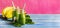 Green smoothies in glass bottles on cool pink blue background with yellow bananas. Panoramic banner with copy space