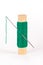 Green spool of thread with a sewing needle on a white background