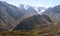 A green spur obscures the river valley among stones and snow-capped peaks in Trans-Ili Alatau