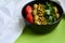 Green summer background and white cloth with  black bowl and delicious useful breakfast of porridge and vegetables. Tomatoes, oliv