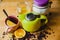 Green teapot on a wooden table. Next to a slice of orange, full cup of tea, honey jar and scattered tea leaves and herbs